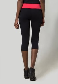 Leggings capri noirs avec une large ceinture rose, confectionnés dans un matériau extensible, présentant une texture lisse et une coupe ajustée.