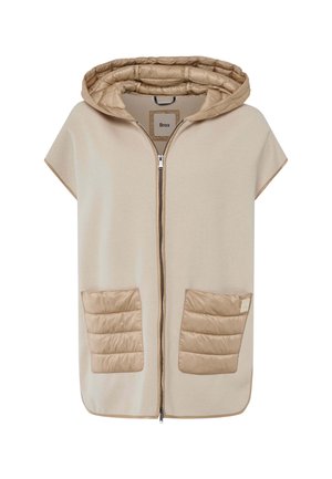 Poncho beige à capuche avec fermeture éclair, présentant des détails de poches matelassées et une texture douce. Les poches ont des motifs cousus pour un détail supplémentaire.