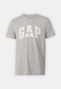 T-shirt en coton gris avec l'inscription « GAP » en blanc, accompagnée d'un détail « Original » en rouge. Col rond, manches courtes, design simple. Texture douce.