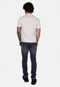 T-shirt bianco a maniche corte abbinato a jeans blu scuro. I jeans hanno una vestibilità classica e tasche posteriori; indossati con scarpe da ginnastica nere.