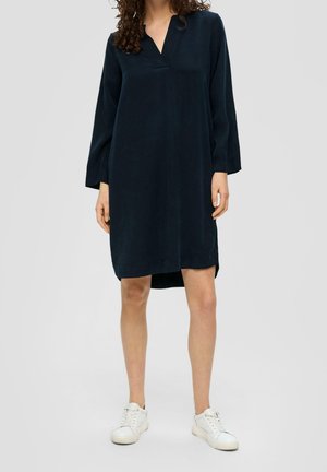 Marineblaues, knielanges Kleid mit V-Ausschnitt und langen Ärmeln. Hergestellt aus weichem Stoff mit seitlichen Schlitzen. Kombiniert mit weißen Sneakers.