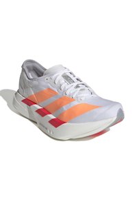 Bílé sportovní boty s oranžovými a růžovými pruhy, textured svršek, tkaničky a zakřivená bílá podrážka s červenými a šedými akcenty.