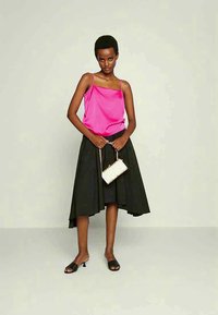 Svetlo roza satenska bluzica na naramnice in črna nabrana midi krila, dopolnjena z majhno belo torbico in črnimi mule čevlji z odprtimi prsti. Gladke teksture in čiste linije.