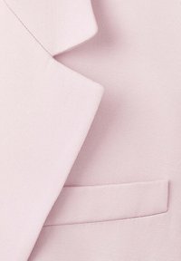 Primer plano de un blazer rosa claro que muestra la tela texturizada, la solapa y el bolsillo de ojal.