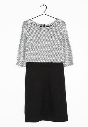 Robe jupe noire avec taille cintrée et haut blanc à motifs avec manches trois-quarts, suspendue sur un cintre noir devant un fond blanc.