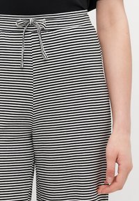 Striped black and white pants with a drawstring waistband and smooth texture, showcasing horizontal lines of varying widths.