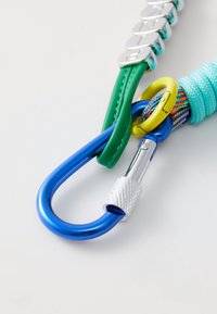 Plavi metalni karabiner povezan sa zelenom kožnom trakicom i žutim metalnim prstenom koji drži više boja pletenu uže sa namotanim svijetloplavim dijelom.