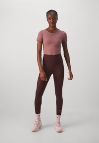 Sportlik riietus, mis sisaldab lühikest mauve värvi T-särki ja kõrge vöökohaga marooni värvi retuuse, millel on õmblusdetailid, koos heleda roosa spordijalatsiga.