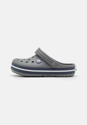 Grå Crocs-tofflor med ventilationshål, en kontrasterande mörknavy rand och en cirkulär logotyp, tillverkade av ett lätt och hållbart material.