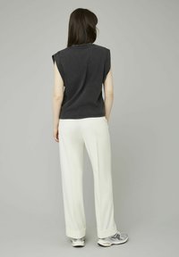 Haut sans manches noir avec une coupe décontractée, associé à un pantalon blanc à jambe large et des baskets grises, vu de dos.