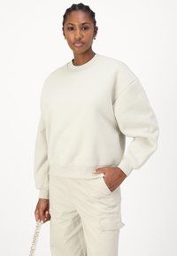 Hellegrauer Sweatshirt mit Rundhalsausschnitt, überschnittenen Schultern und gerippten Bündchen. Kombiniert mit cremefarbenen Cargo-Hosen.