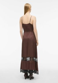 Bruine satijnen maxi-jurk met dunne schouderbandjes, voorzien van zwarte kantpanelen aan de zoom. Het ontwerp is elegant met een zachte textuur.