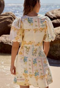 Kwiatowa sukienka z bufkami, z żółtym tłem i niebieskimi, różowymi oraz zielonymi wzorami kwiatowymi w stylu patchwork.