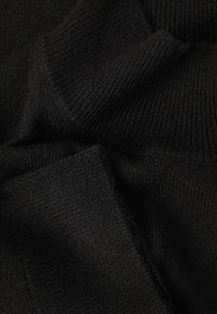 Tissu en tricot noir avec une texture côtelée, montrant des plis et des couches, indiquant douceur et chaleur. Pas de motifs visibles ni d'accents notables.