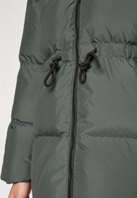 Giacca imbottita di colore grigio scuro con una finitura liscia, dotata di zip frontale, regolatori con coulisse in vita e polsini elasticizzati.