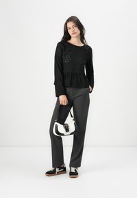 Top lungo a maniche nere con texture e design a peplo, abbinato a pantaloni grigi e una borsa bicolore. Sneaker nere con dettagli bianchi completano il look.