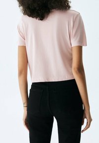 T-shirt rosa tagliata realizzata in tessuto morbido con maniche corte, abbinata a jeans neri a vita alta. Design minimalista, senza motivi visibili.