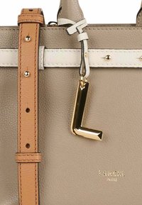 Sac à main en cuir beige avec des anses brunes et blanches, quincaillerie dorée et un charm en forme de "L" doré. Présente un logo embossé près de la base.