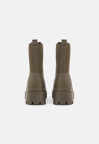 Botas de tobillo verdes con un acabado mate, que cuentan con paneles laterales elásticos, una suela gruesa y lengüetas para ponerlas y quitarlas fácilmente.
