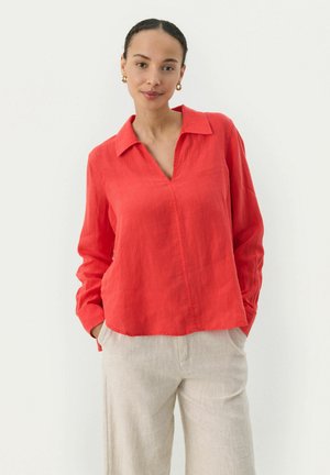 Red, long-sleeve linen blouse with a notch collar and side pockets, paired with light beige linen pants. Simple, casual design.