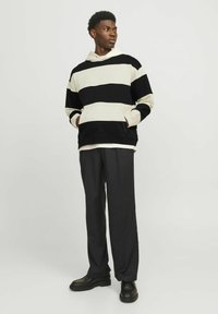 Hoodie noir et crème rayé avec une poche avant, associé à un pantalon noir ample et des chaussures noires à lacets.