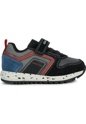 Scarpa da ginnastica nera e grigia con accenti rossi, camoscio blu e suola bianca punteggiata distintiva. Presenta una fascia in velcro e dettagli testurizzati.