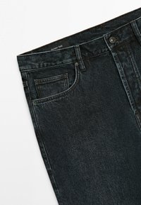 Sorte denimjeans med forlommer, bæltestropper, metal knaplukning og synlig "Massimo Dutti" indvendig label ved linningen.