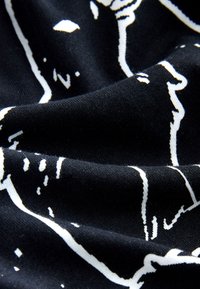 Czarna tkanina o miękkiej fakturze, zdobiona białym abstrakcyjnym wzorem na całej powierzchni. Materiał wydaje się rozciągliwy i gładki.