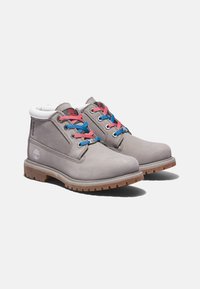 Botas de cuero gris hasta el tobillo con cuello blanco, cordones azules y rosas, suela de goma y detalle del logo. Presentan una construcción resistente y un diseño impermeable.