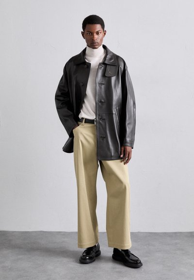 Sorte læderjakke med en bred krave, knaplukning og frontlommer, båret over en cremefarvet turtleneck og beige vidde ben-bukser. Sorte sko.