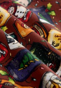 Geweven stof met een bruine achtergrond en feestelijke illustraties van kaarsen, kerstbomen en feestverlichting in verschillende kleuren.