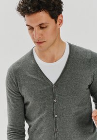 Szary, dziergany kardigan z dekoltem w kształcie litery V, z pięcioma guzikami z przodu i miękką teksturą, nałożony na biały T-shirt.