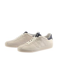 Beige leather sneakers with a textured finish, featuring a white rubber sole, contrasting dark navy heel, and decorative buckle detail.