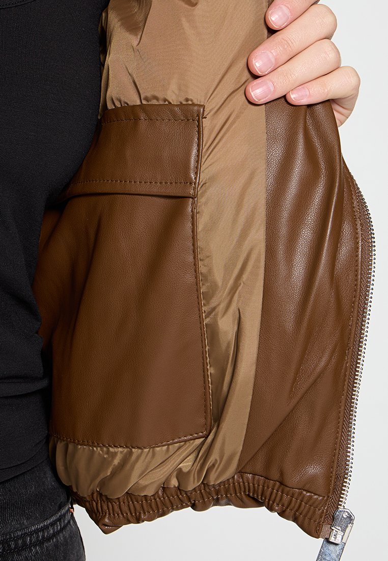 Brązowa skórzana kurtka z beżowym nylonowym podszewką. Posiada boczną kieszeń i elastyczne mankiety, eksponując gładkie faktury i dopasowany krój.