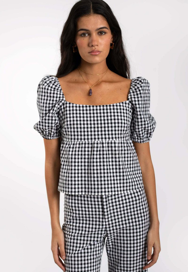 Haut à carreaux noir et blanc avec des manches courtes bouffantes, décolleté carré et design peplum, associé à un pantalon à carreaux assorti.