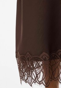 Brūnas krāsas kleita ar gludu tekstūru, tās apakšmalā izšūts detaļains mežģīņu raksts ar ziedu motīviem un bārkstīm.