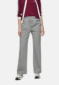 Graue, breitbeinige Hose mit Nadelstreifen, elastischem Bund und Kordelzug. Kombiniert mit einem burgunderroten Oberteil, einer Jacke mit weißen Akzenten und Sneakers.