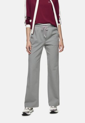 Graue, breitbeinige Hose mit Nadelstreifen, elastischem Bund und Kordelzug. Kombiniert mit einem burgunderroten Oberteil, einer Jacke mit weißen Akzenten und Sneakers.