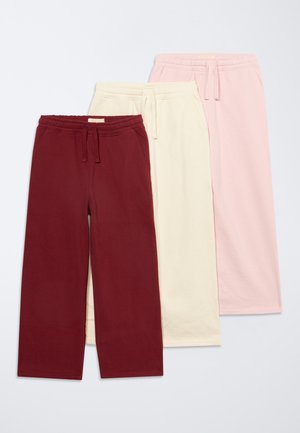 Trois paires de pantalons de survêtement à jambes larges en bordeaux, crème et rose clair, chacun avec une taille élastique et un cordon.