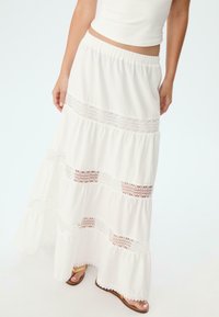 Jupe maxi blanche avec un design en couches, des accents en dentelle et un ourlet volanté. Fabriquée dans un matériau léger avec une taille élastique.