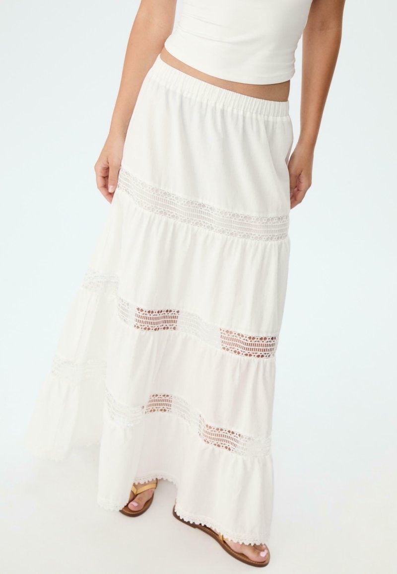 Jupe maxi blanche avec un design en couches, des accents en dentelle et un ourlet volanté. Fabriquée dans un matériau léger avec une taille élastique.