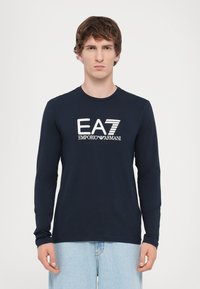 Marineblå langermet t-skjorte i bomull med rund hals. Har hvit EA7 Emporio Armani-logo over brystet. Jevn tekstur.