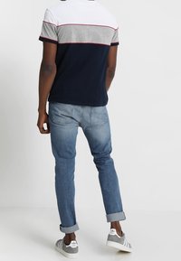 Camisa de manga corta en azul marino, gris y blanco con rayas horizontales. Combinada con jeans de tiro bajo azul claro con los puños doblados y zapatillas grises.