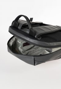 Zaino nero con finitura opaca liscia, dotato di apertura con zip e un interno morbido e chiaro. Due maniglie robuste sulla parte superiore.