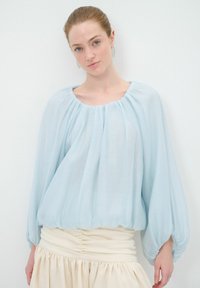 Himmelbluse aus leichtem, luftigem Stoff mit weitem Ausschnitt und elastischen Bündchen, kombiniert mit einem cremefarbenen, gerafften Rock mit Taillengummi. Weicher, transparenter Stoff.