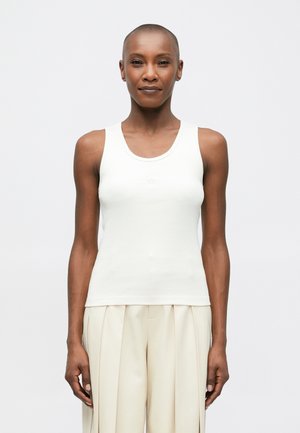 White ribbed tank top with a round neckline, featuring a fitted design. Paired with light beige high-waisted pleated trousers.