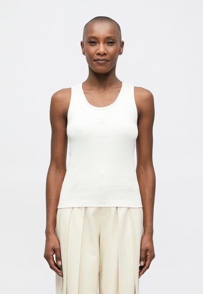 Witte geribde tanktop met een ronde halslijn, featuring een getailleerd ontwerp. Gecombineerd met lichtbeige hoog waisted geplooide broeken.