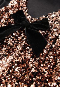 Top z bleščicami iz črnega blaga, okrašen z množico odsevnih bakreno obarvanih bleščic. Vključuje detajl črnega žametnega traku na izrezu.