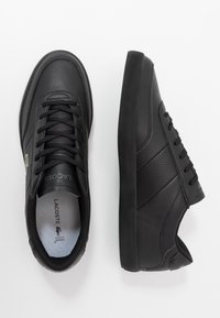 Paire de baskets Lacoste noires avec lacets, une chaussure vue de dessus et l'autre de côté sur fond blanc.