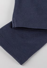 Tessuto di cotone blu scuro con una consistenza liscia. Presenta orli cuciti in modo ordinato, polsini ripiegati e un design semplice senza motivi o accenti.